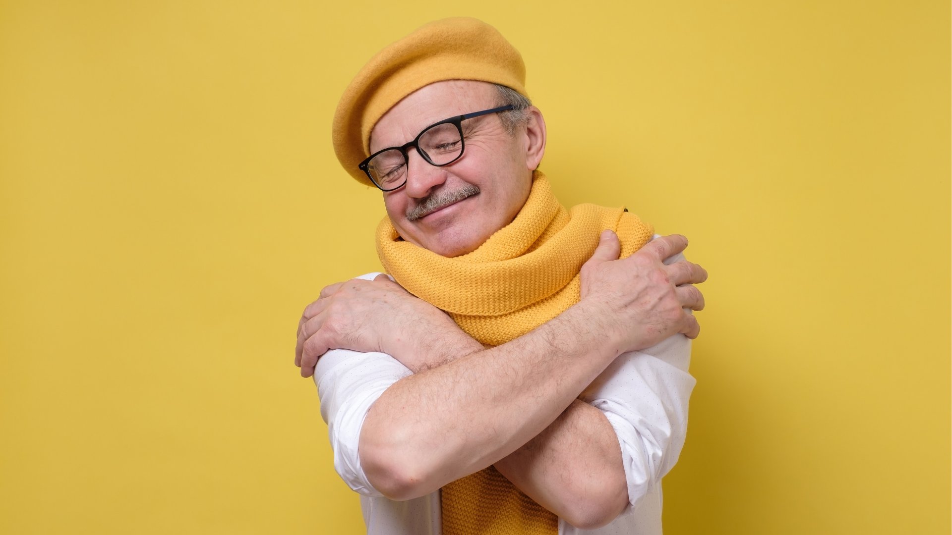 Senhor usando boina e cachecol amarelo se abraça