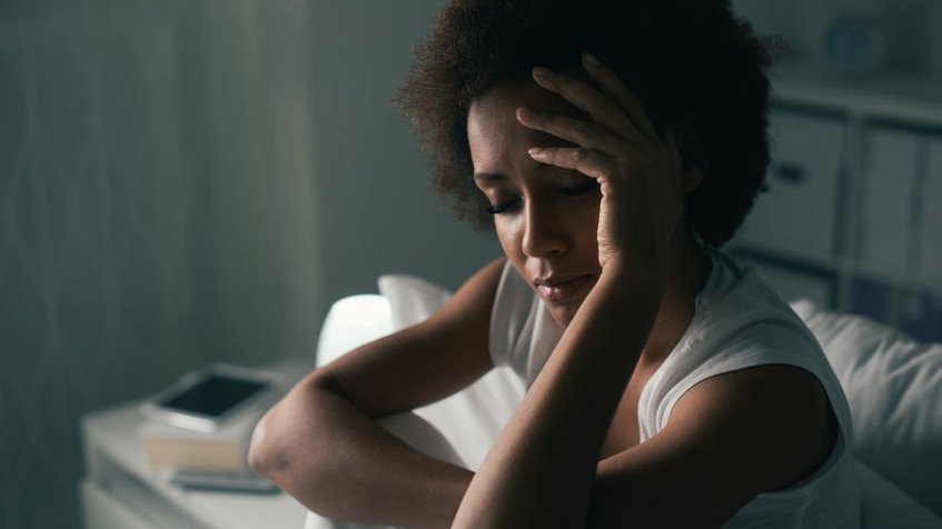 Mulher triste e deprimida sentada na cama e tocando a testa