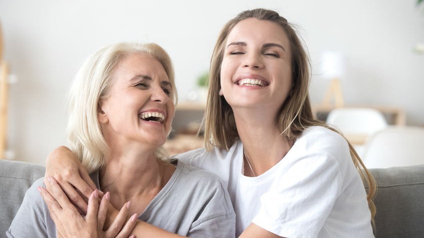 Mulher abraçada com idosa e sorrindo