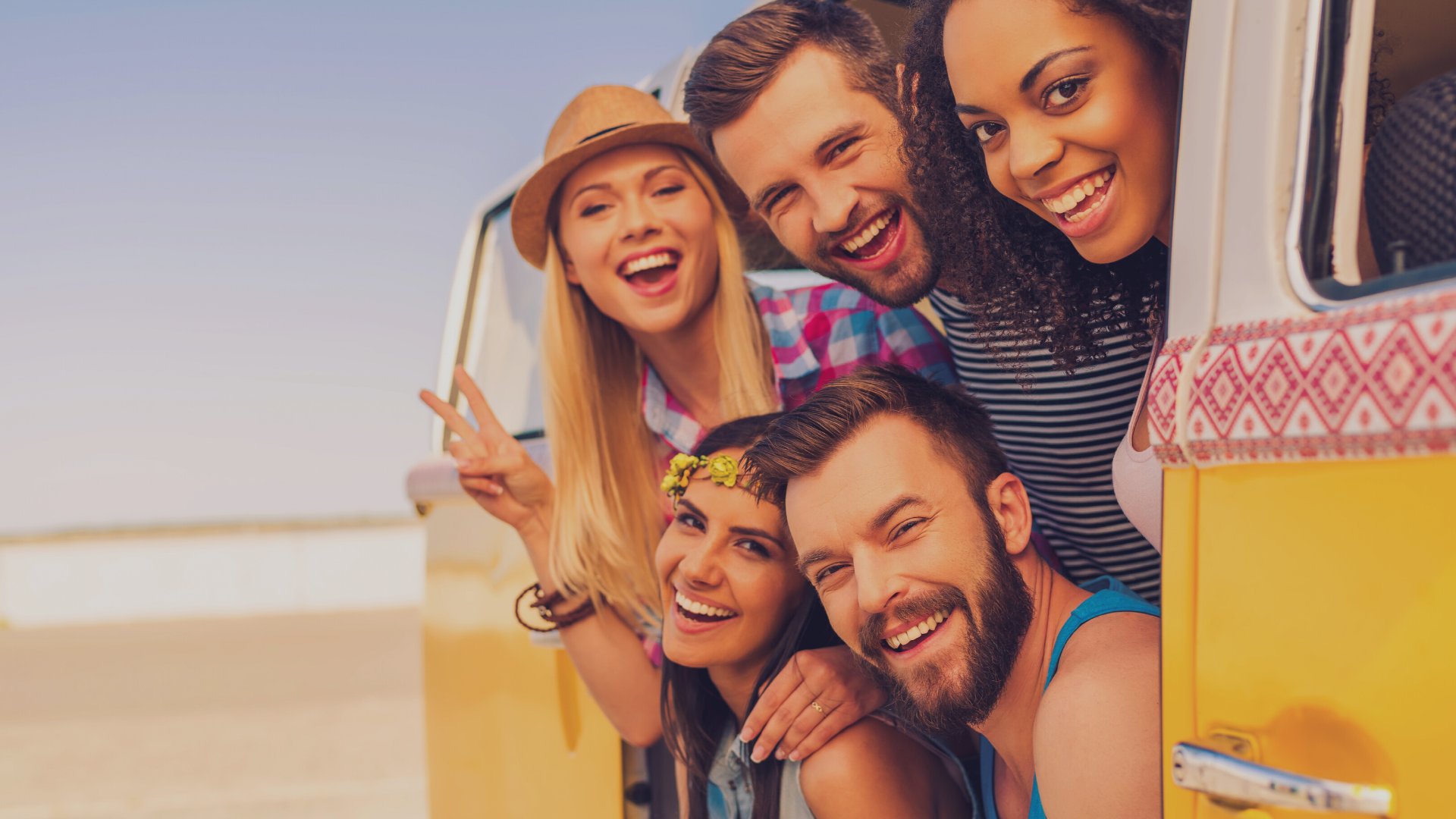 G-stockstudio / Getty Images Pro / Canva Grupo de amigos em um carro com o mar ao fundo.