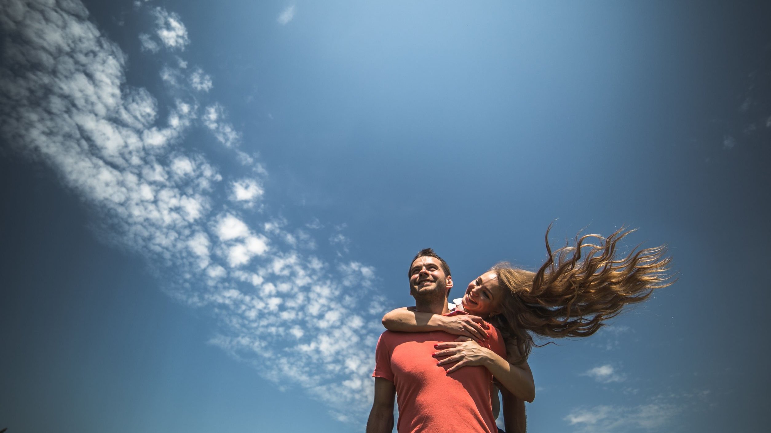 Mulher abraça homem em um cenário de céu azulado