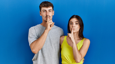 Krakenimages.com / Shutterstock Homem e mulher fazendo sinal de silêncio com o dedo.