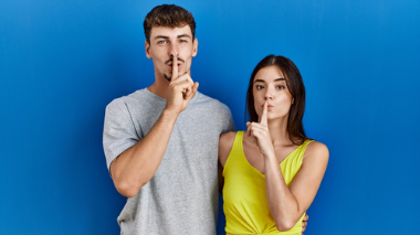 Homem e mulher fazendo sinal de silêncio com o dedo.