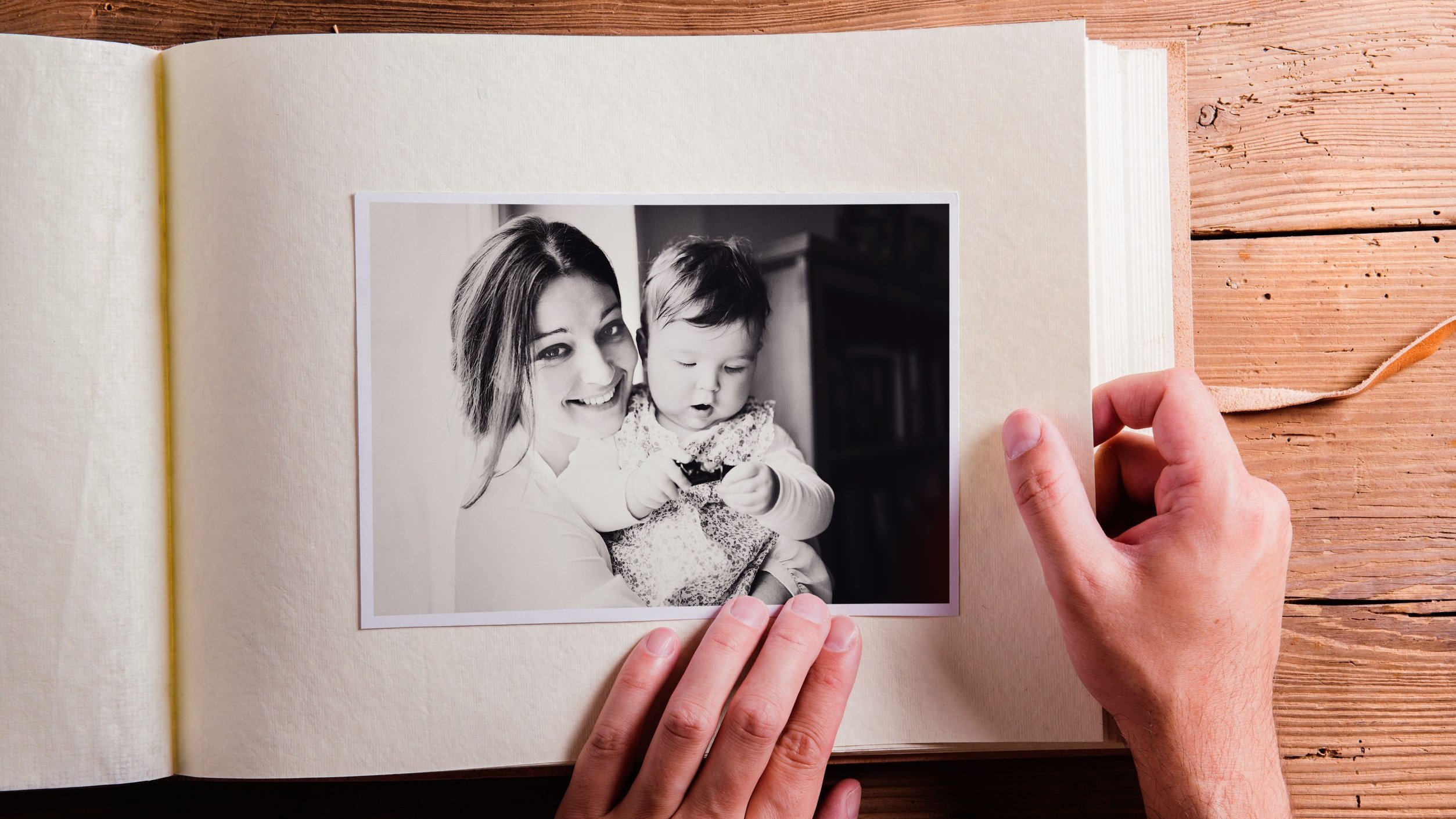 Mãos sobre um álbum de fotos antigas, com uma foto de uma mãe segurando seu filho no colo