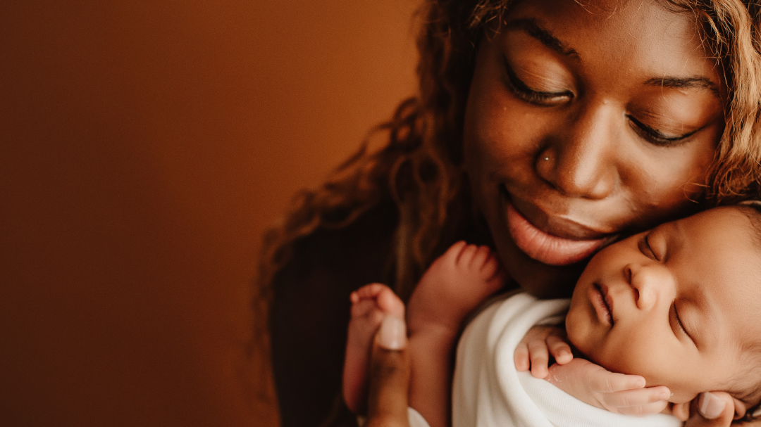 Foto de uma mãe negra segurando seu bebê com o rosto encostado no rosto dele.