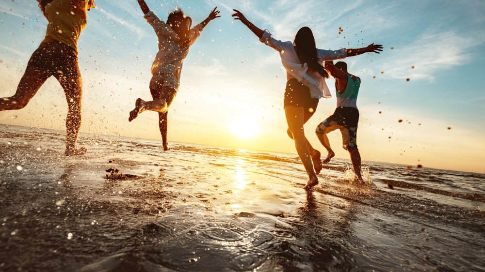 Quatro amigos felizes na festa ao pôr do sol na praia