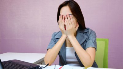 Mulher sentada em uma mesa de escritório com as mãos sobre o rosto.