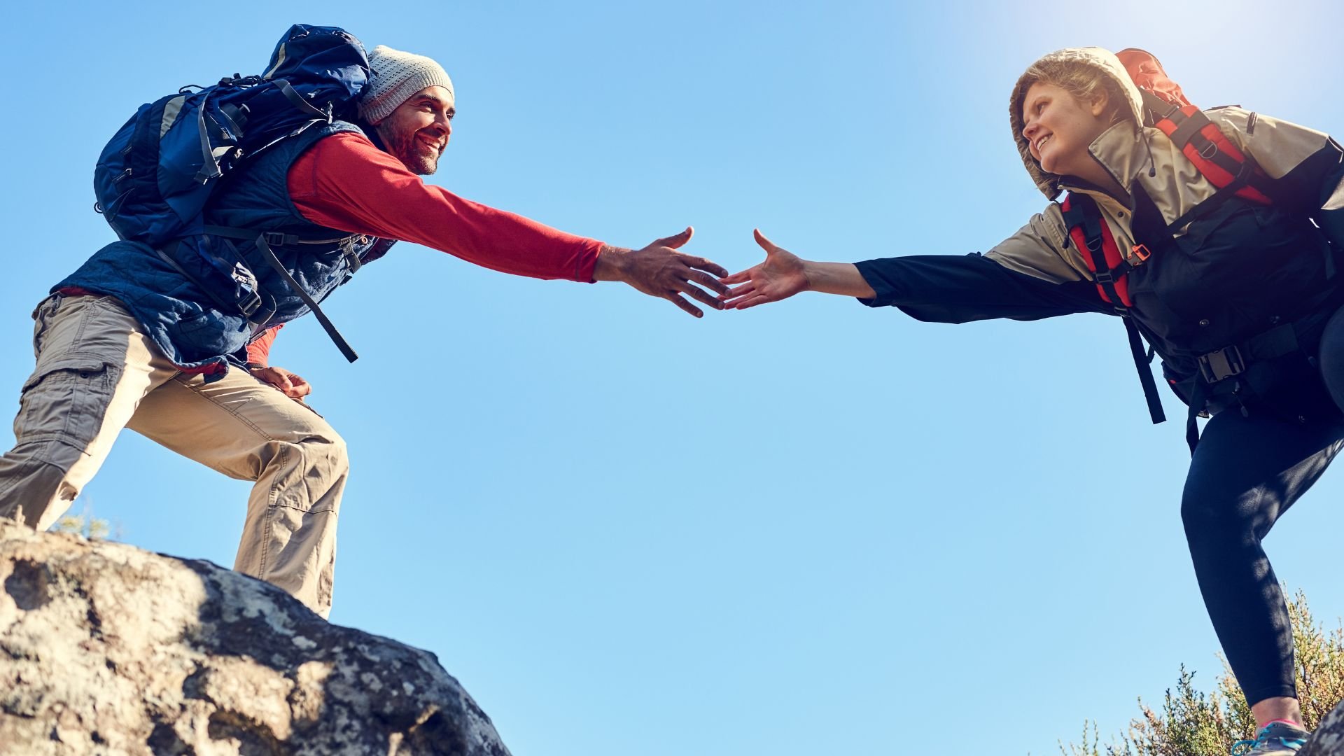 Imagem de um homem e uma mulher se ajudando a passar passar de um lado da pedra de uma montanha para a outra