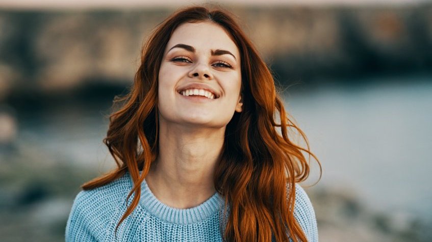 Mulher branca de cabelos ruivos sorrindo.