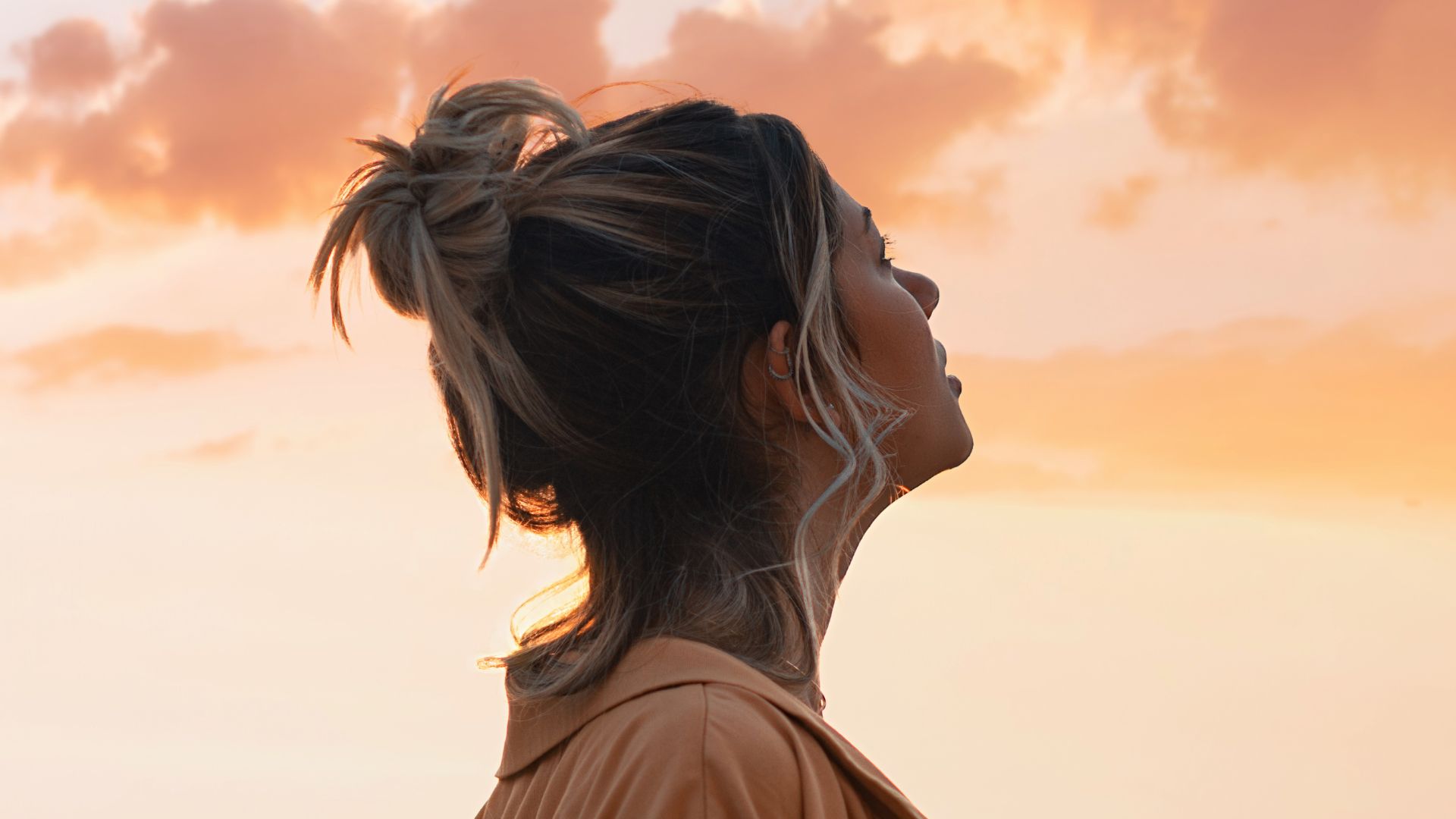 Imagem de uma mulher de perfil olhando para o céu alaranjado como se estivesse refletindo.