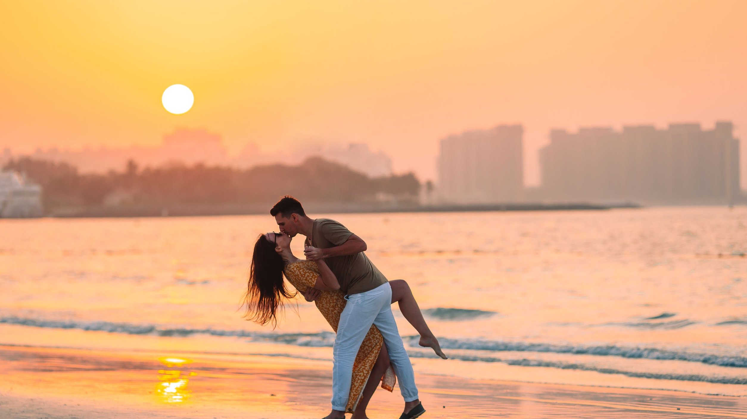 Homem e mulher se beijando em praia durante o pôr-do-sol.