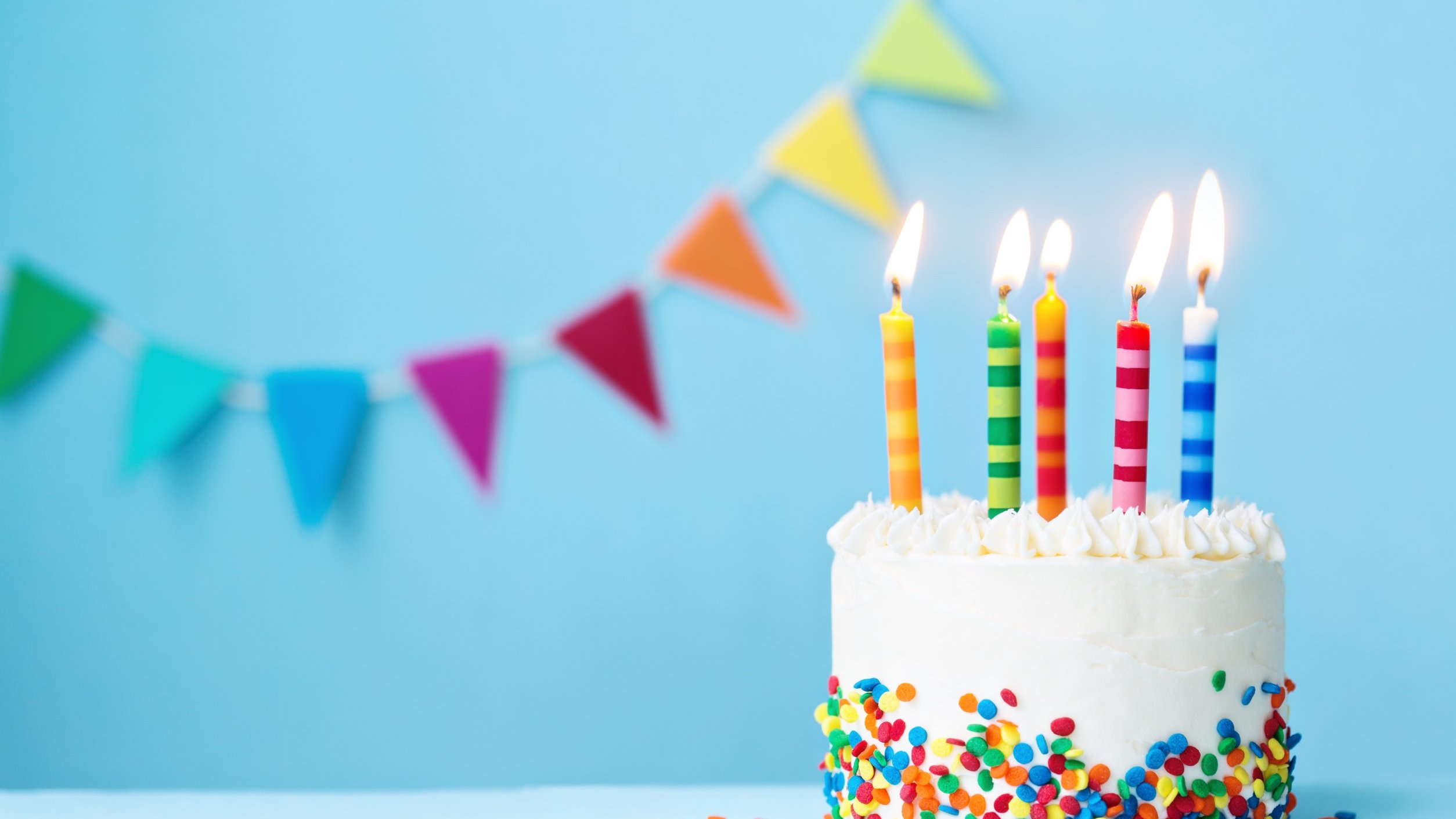 Bolo de aniversário com velas acesas e bandeirinhas no fundo