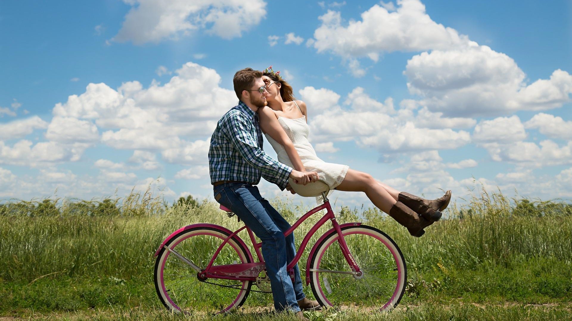 Um casal feliz andando em uma bicicleta por uma trilha e o dia está ensolarado.