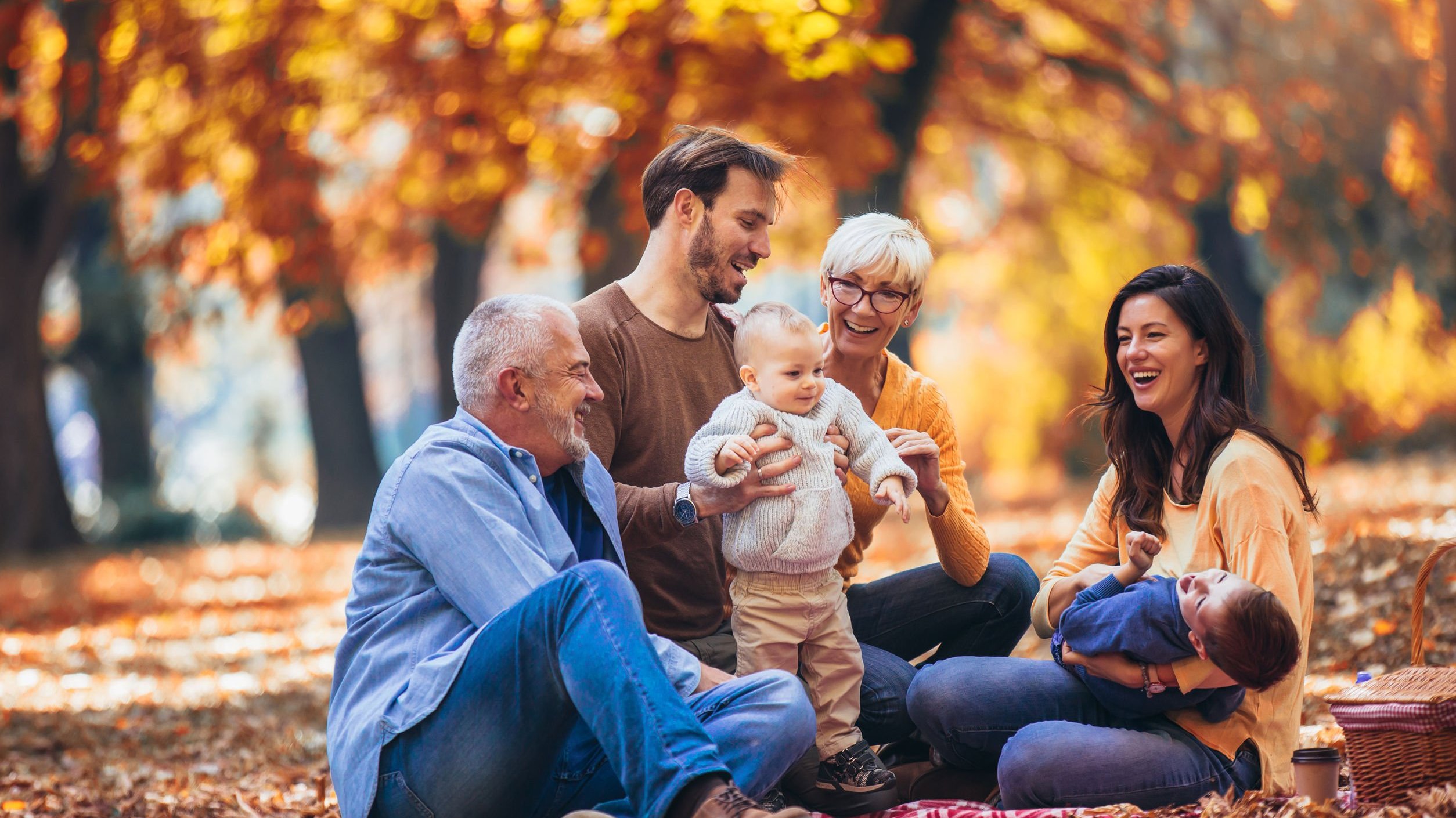 Família composta de por idosos, adultos e crianças em um cenário outonal