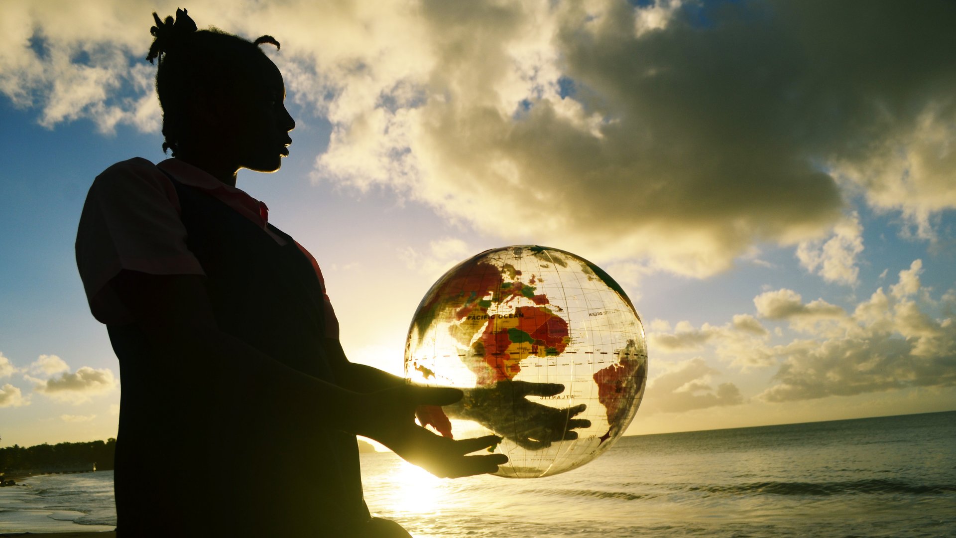 Silhueta de mulher segurando o globo terrestre enquanto admira o pôr do sol