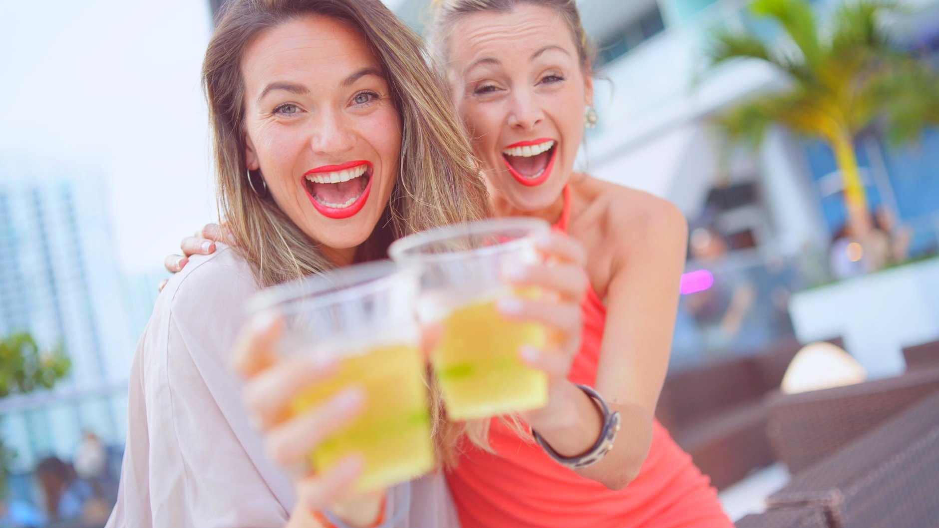 Duas mulheres brancas brindando copos, com expressões sorridentes.