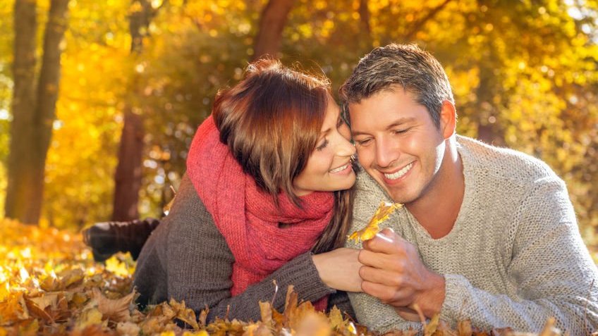 Casal sorrindo e folhas alaranjadas ao redor