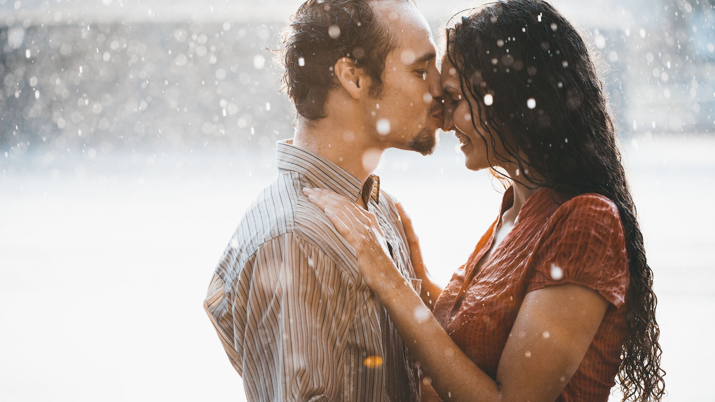 Homem beija mulher na testa em meio à chuva