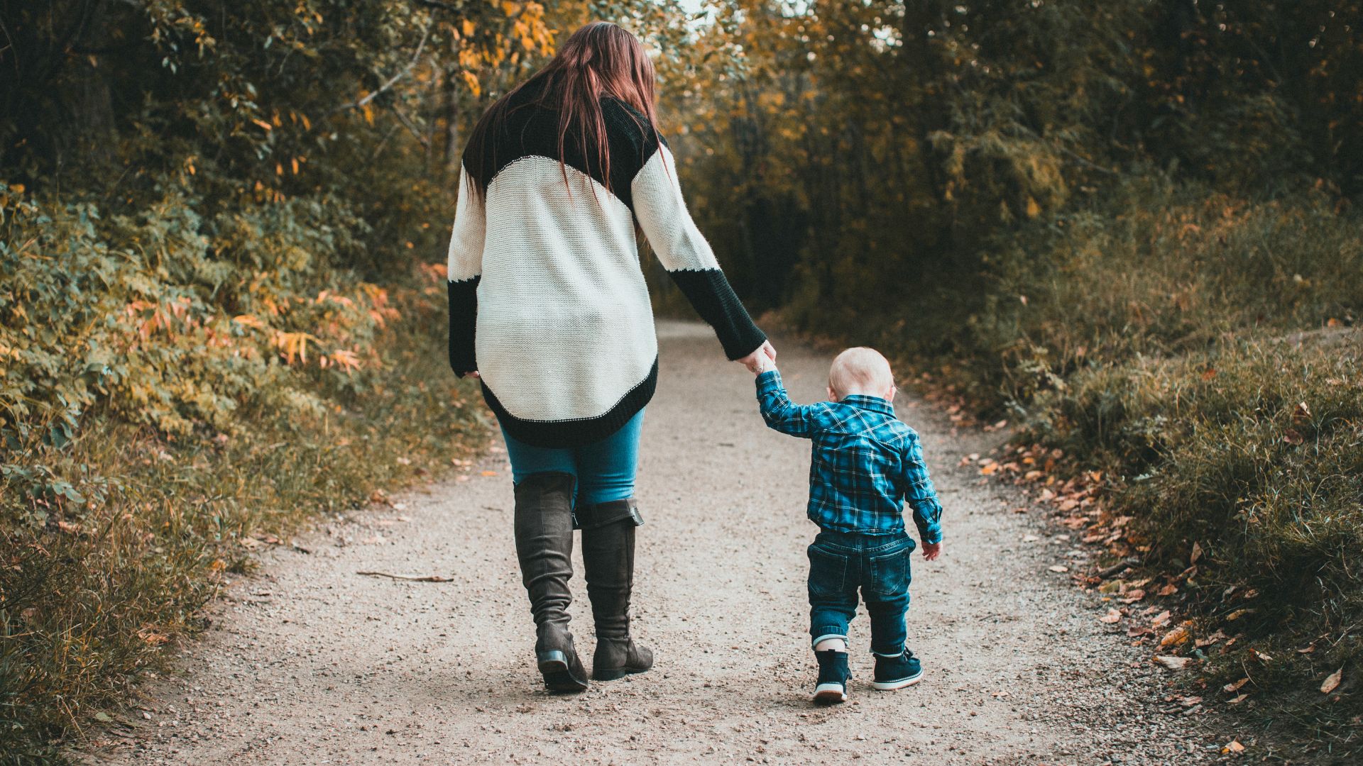 Imagem de uma estrada de areia. Tia e sobrinho caminham de mãos dadas sobre ela.