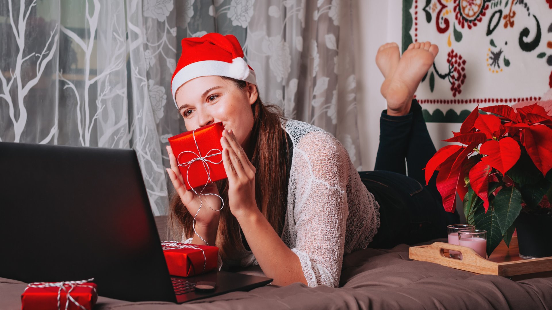 Mulher no natal deitada na cama mostrando um presente para o computador