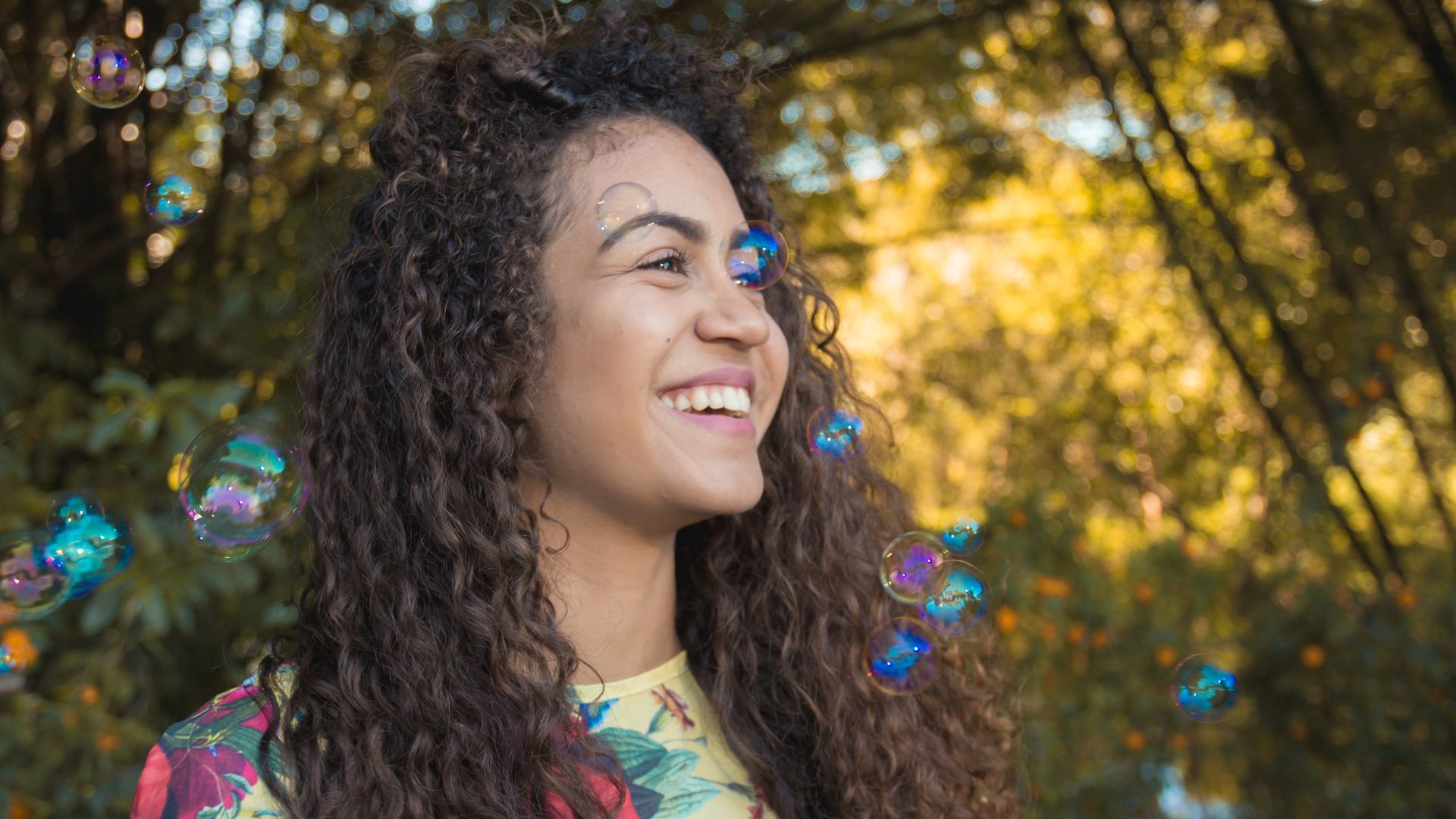 Nappy de Pexels grátis para o Canva Pro Mulher de cabelos longos e cacheados, sorrindo. Bolinhas de sabão complementam a imagem.