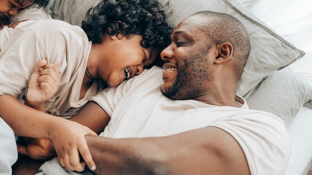 Um menino e um homem deitados na cama brincando e rindo.