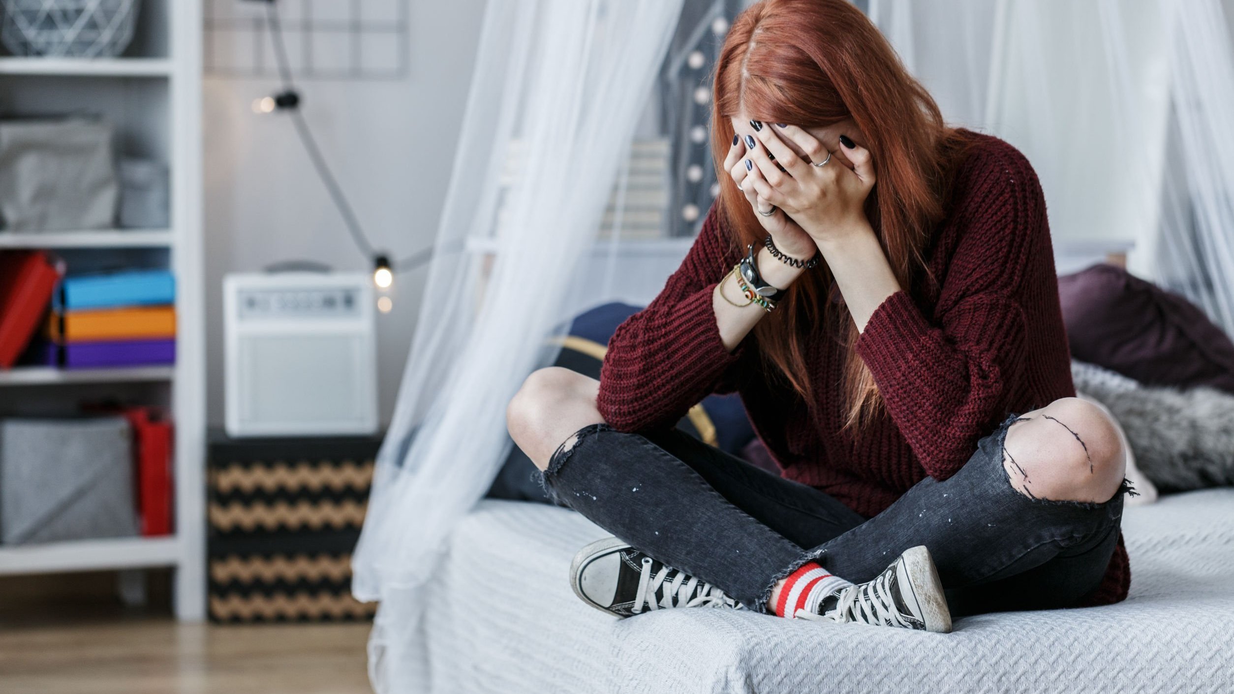 Jovem sentada na cama triste