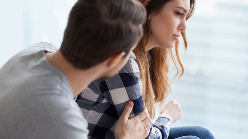 Mulher com olhar triste e homem com a mão no braço dela em consolo