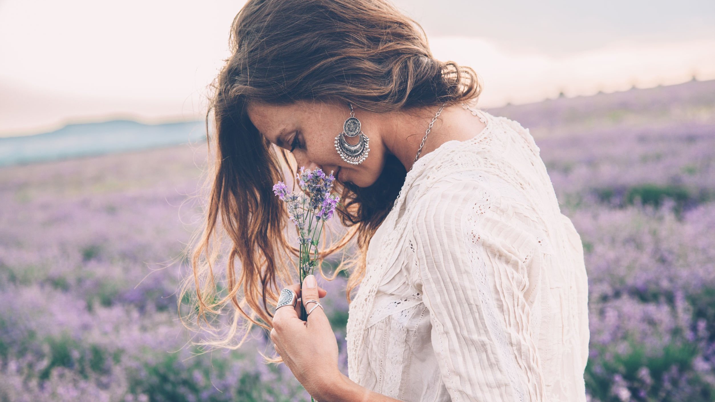 Mulher em um campo de flores, segurando uma flor e a cheirando