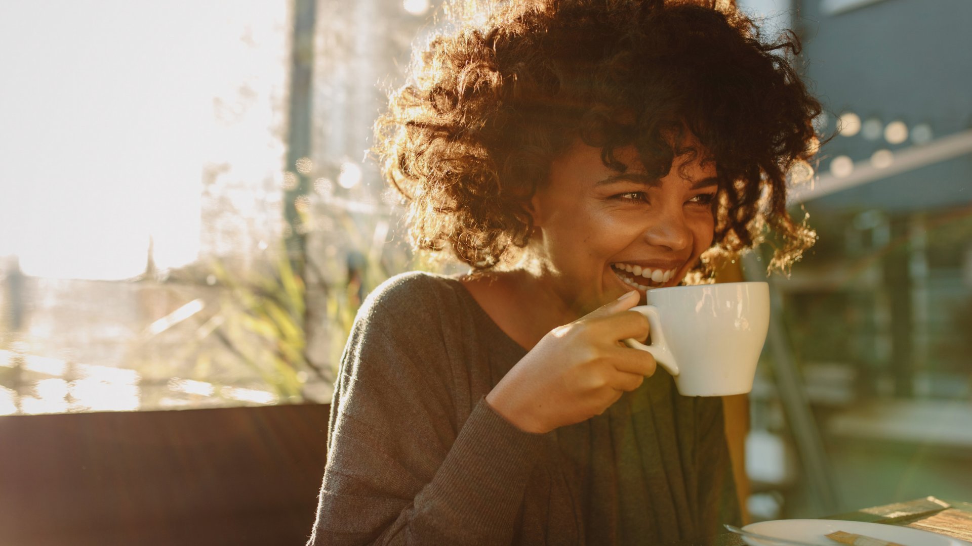 Jacob Lund / Canva Mulher sentada em um café sorrindo enquanto toma uma xícara de café
