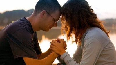 Casal de mãos dadas e olhos fechados, em sinal de oração