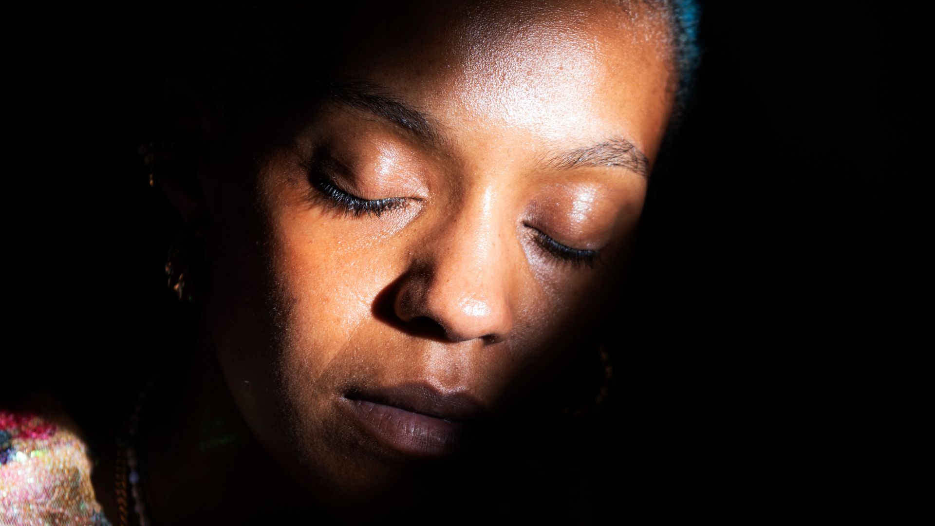Imagem de uma mulher com os olhos fechados em um fundo preto e apenas seu rosto iluminado