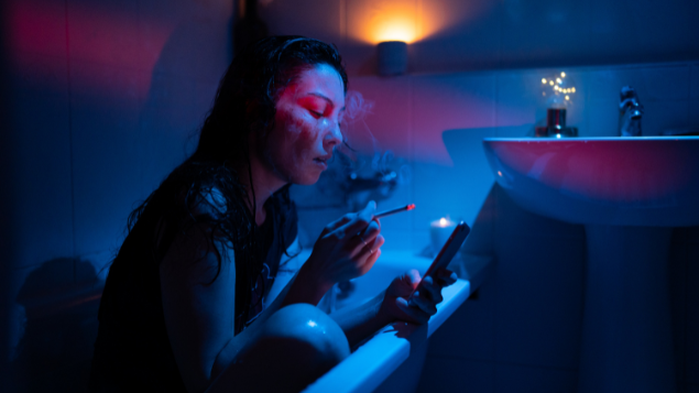 Dmitry Marchenko / EyeEm de Getty Images Mulher triste mexendo no celular enquanto está dentro da banheira fumando um cigarro.
