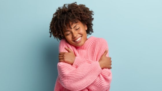 Mulher sorrindo e abraçando a si mesma.