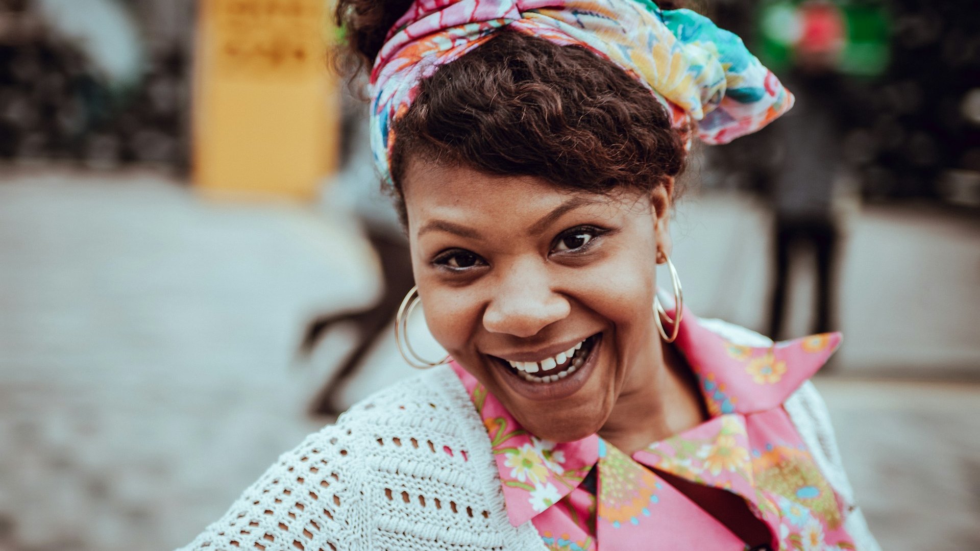 Mulher negra sorridente na rua, com roupas coloridas.