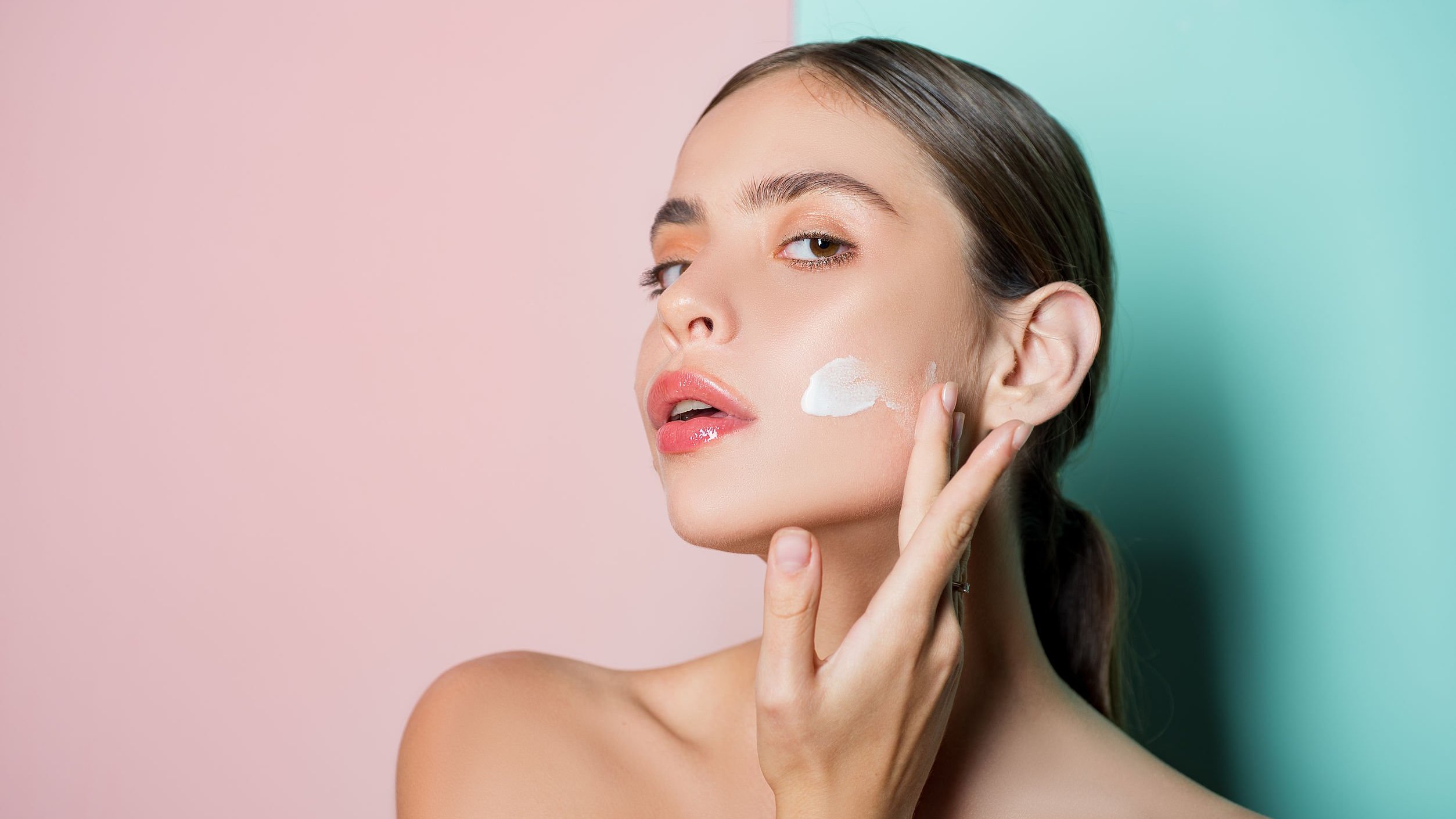 Retrato de uma linda jovem tocando a bochecha com a mão, aplicando creme facial.