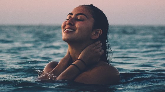 Mulher sorrindo no mar com os olhos fechados