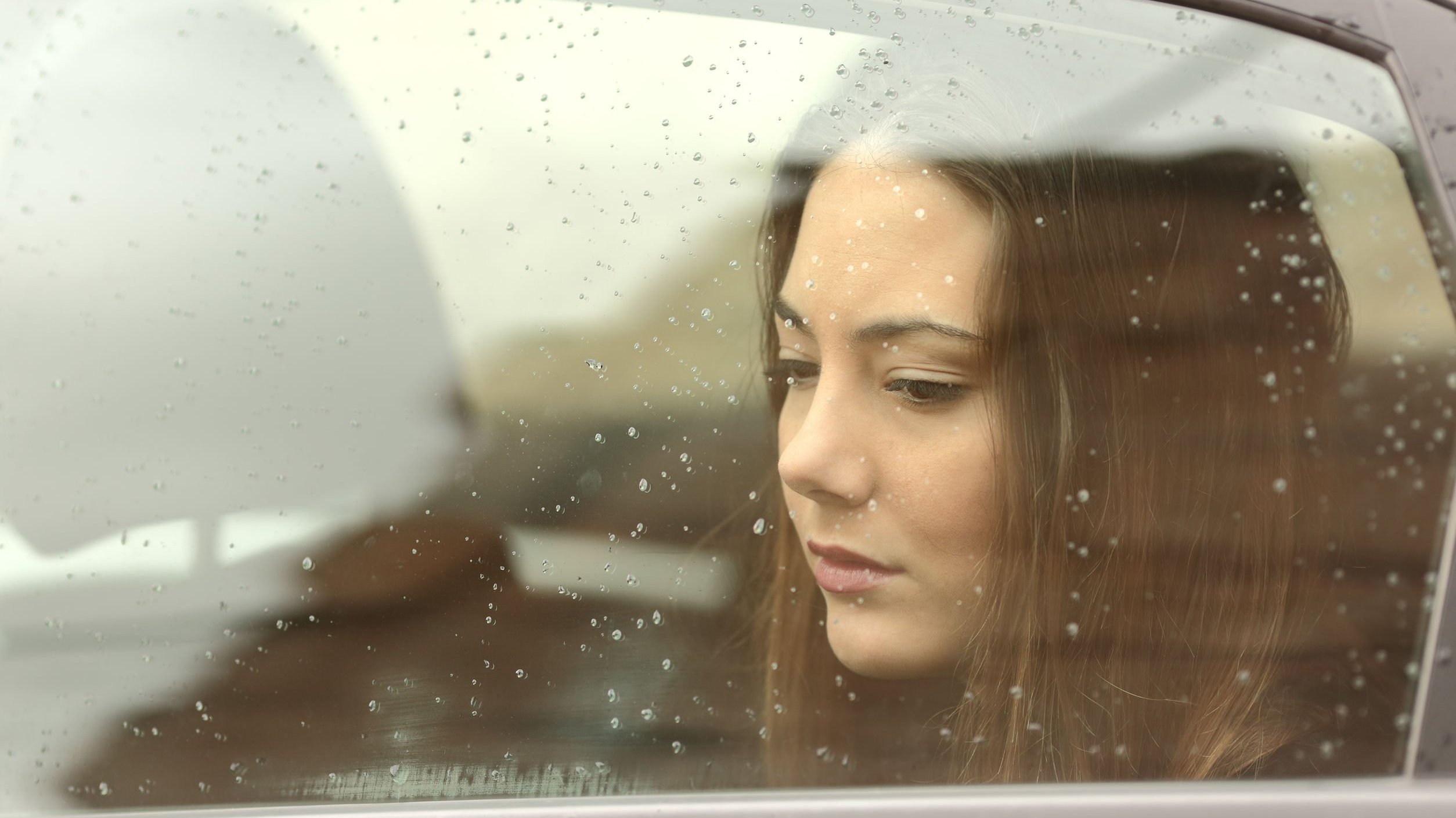 Mulher sentada na janela de um carro com olhar triste.