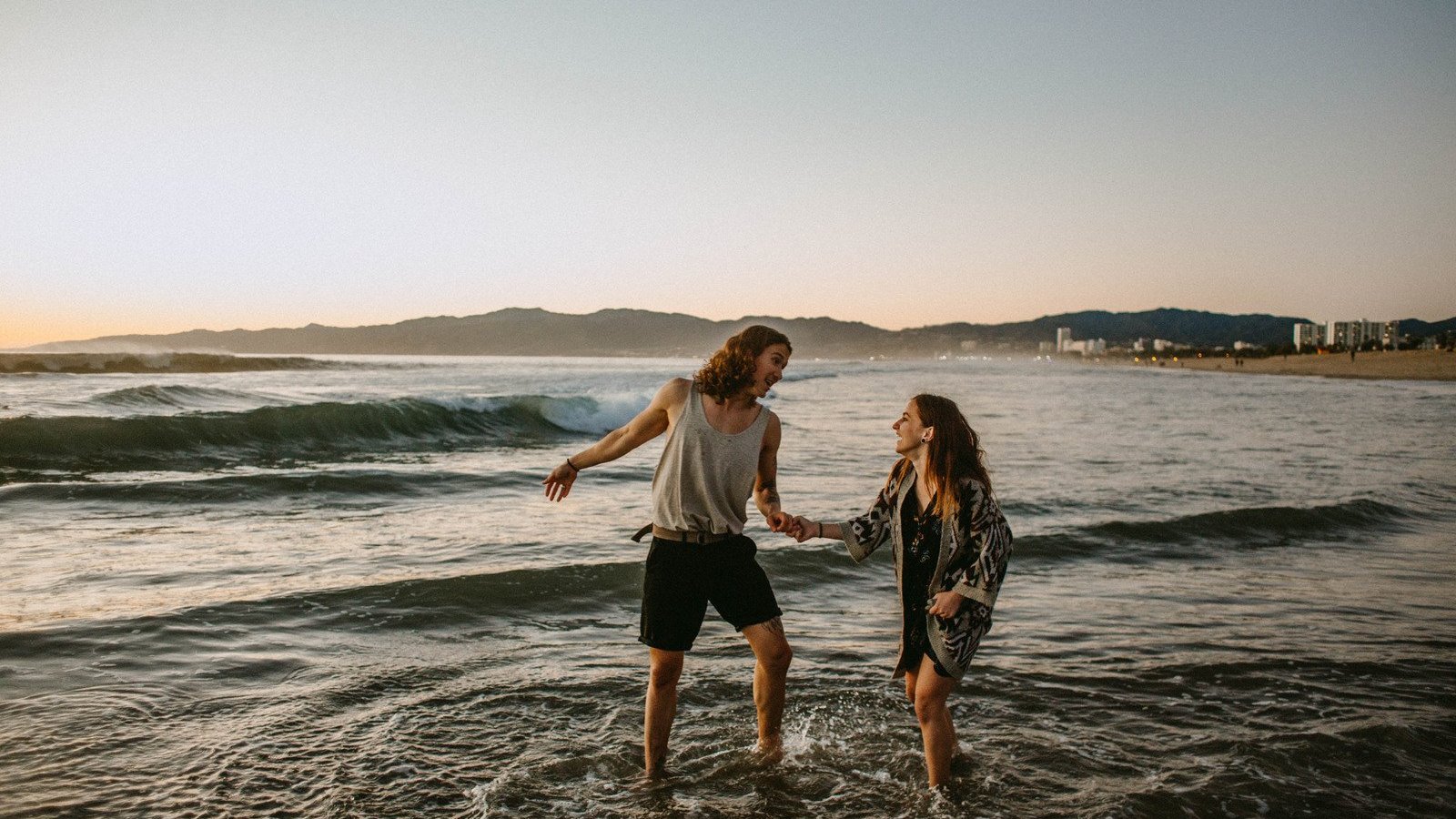 Valeria Ushakova / Canva PRO Homem e mulher brancos, de mãos dadas na beira do mar.