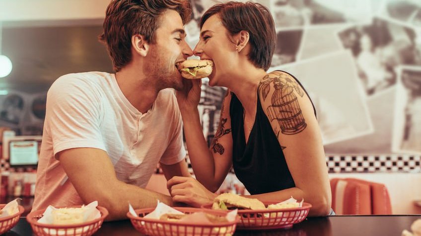 Casal feliz em um restaurante comendo um hambúrguer juntos, olhando um para o outro.