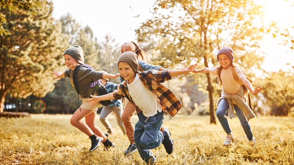 Crianças sorrindo e correndo de braços abertos ao ar livre