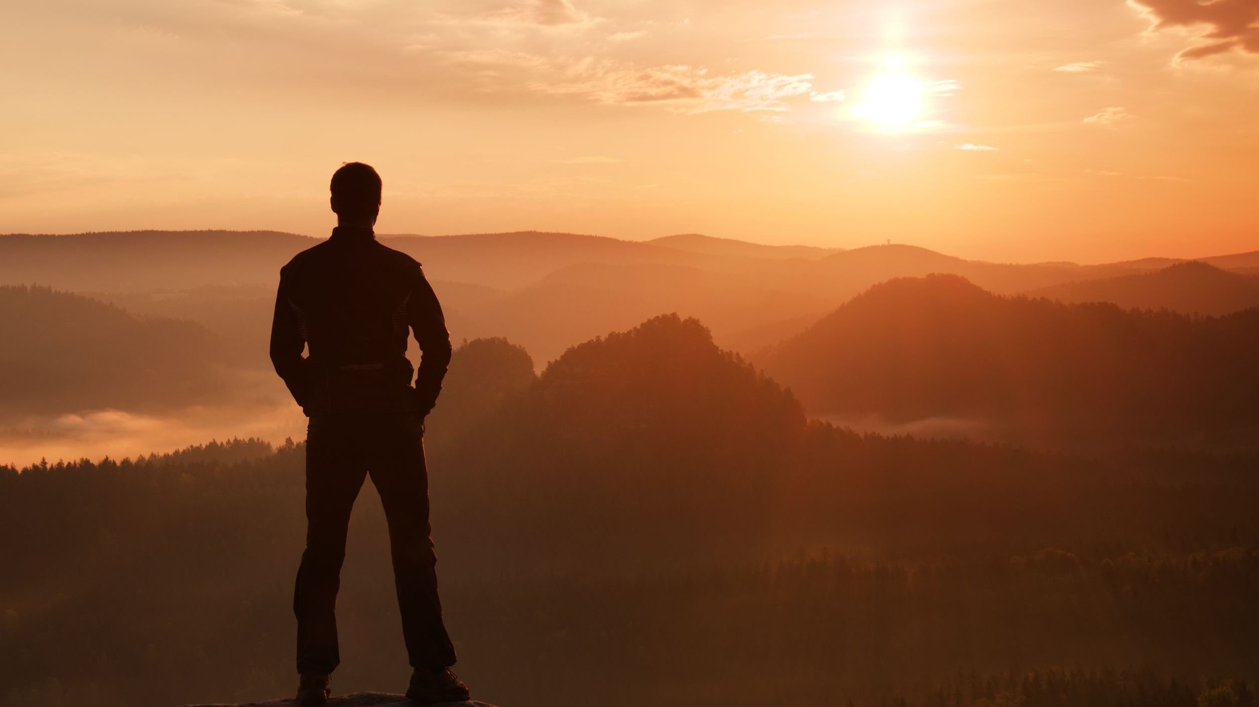 Silhueta de um home olhando para o sol no topo da montanha