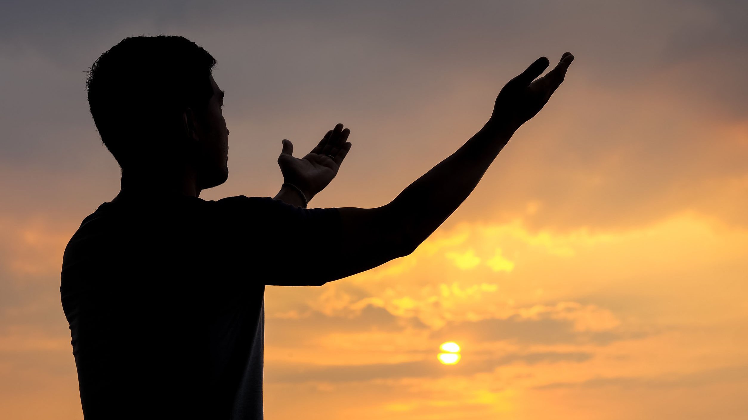 Silhueta de um homem com braços abertos ao pôr do sol