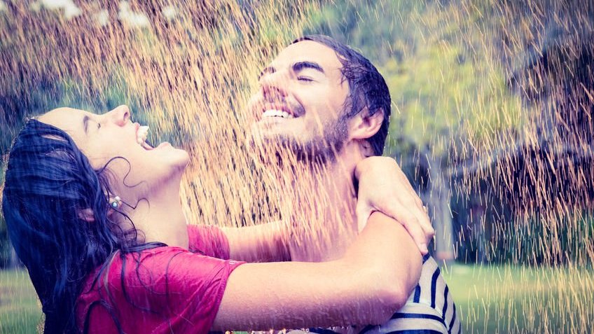 Casal abraçado sorrindo tomando chuva