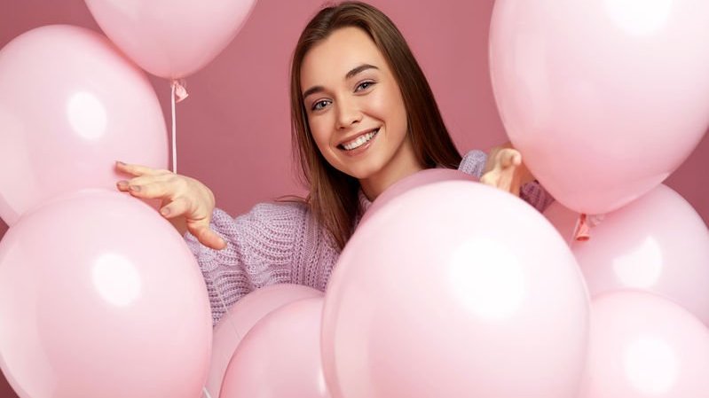 Menina sorrindo entre balões rosa.
