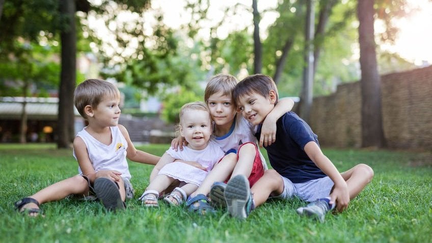 Quatro crianças abraçadas sorrindo na grama
