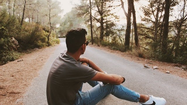 Homem sentado em estrada com floresta dos lados