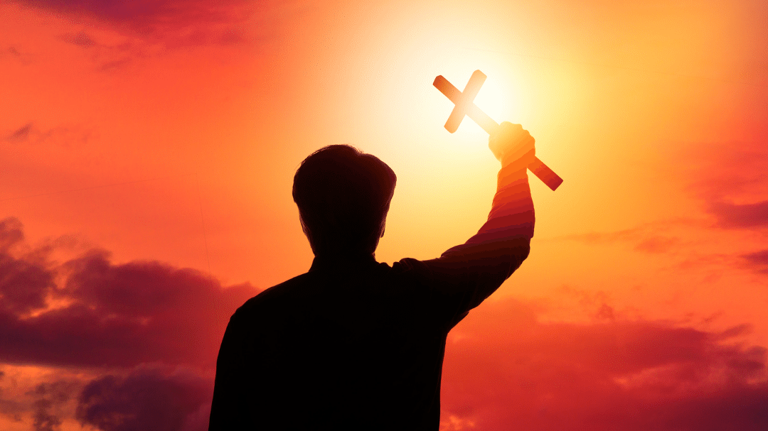 Homem segurando uma cruz e ao fundo, o céu alaranjado.
