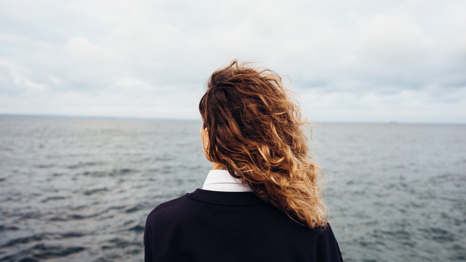 progressman / Canva PRO Mulher branca de costas enquanto observa o mar.