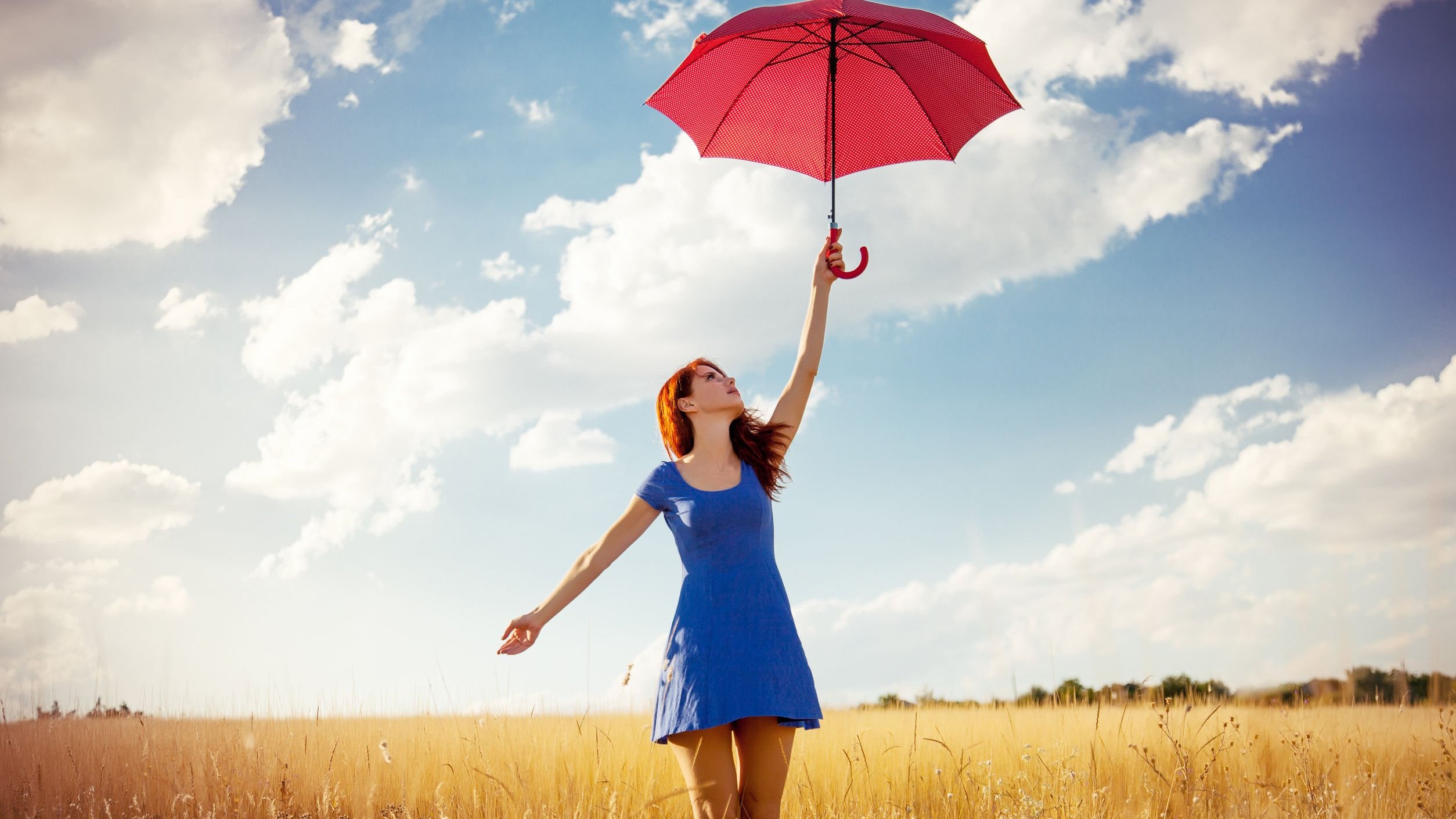 Mulher branca e ruiva segurando guarda-chuva num campo.